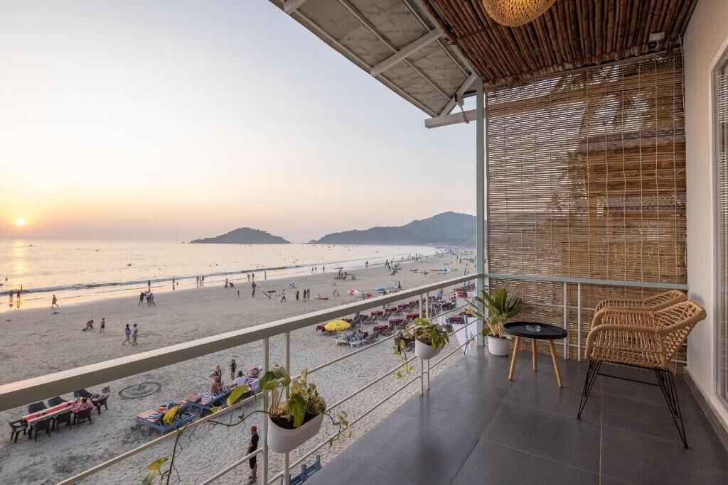 A balcony with a view of the beach and ocean, outdoor seating, and potted plants.