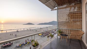 A balcony with a view of the beach and ocean, outdoor seating, and potted plants.