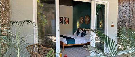 A bedroom with a bed, a glass door leading to a balcony, and a view of the outdoors.