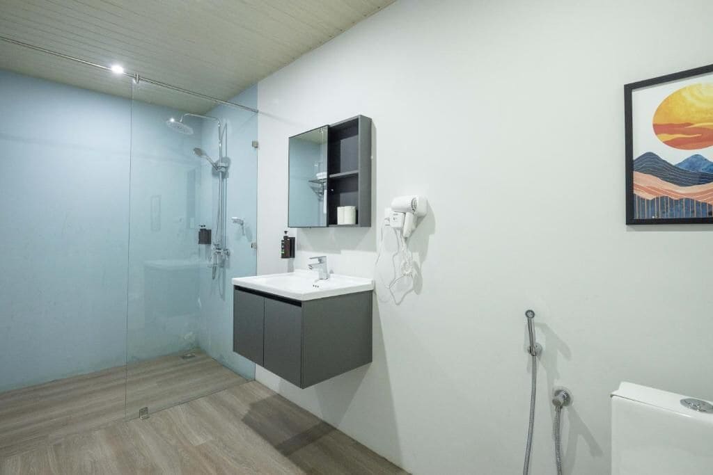 Un baño moderno con cabina de ducha de vidrio, un lavamanos blanco, un mueble oscuro y un espejo montado en la pared.