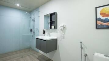 Un baño moderno con cabina de ducha de vidrio, un lavamanos blanco, un mueble oscuro y un espejo montado en la pared.