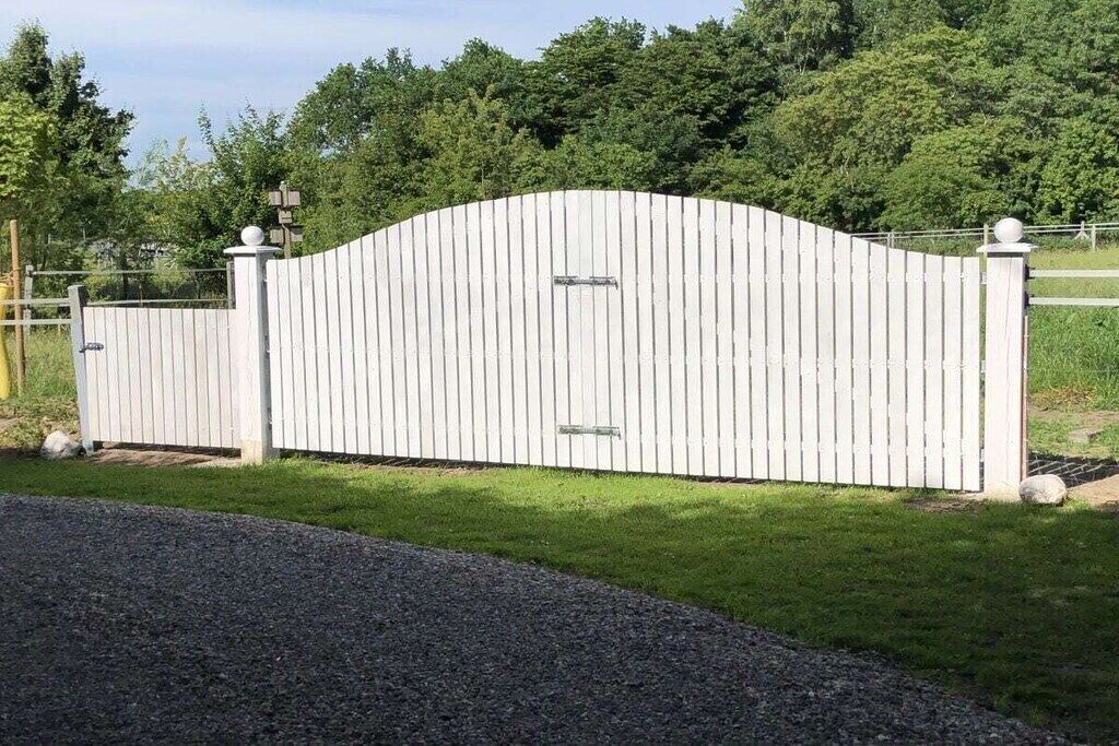 A white metal gate with a curved top and two posts with spherical finials.