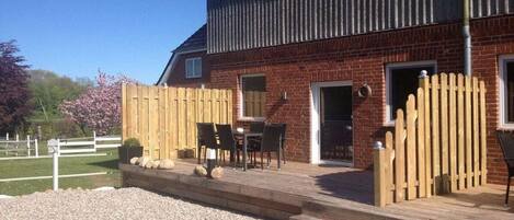 A brick building with a wooden deck, outdoor seating, and a fenced area.