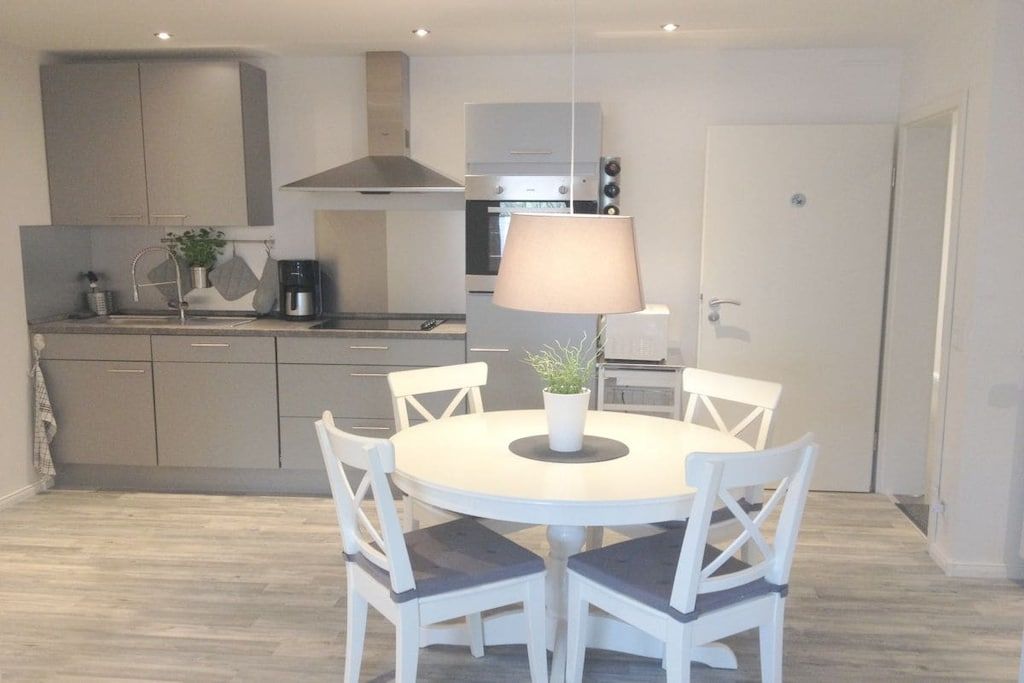 A modern kitchen with a round dining table and white chairs, a built-in oven, and a stove.