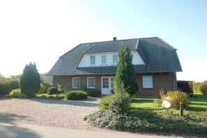 Ein zweistöckiges Haus mit Satteldach, einer Veranda und einer Zuwegung mit Kies.