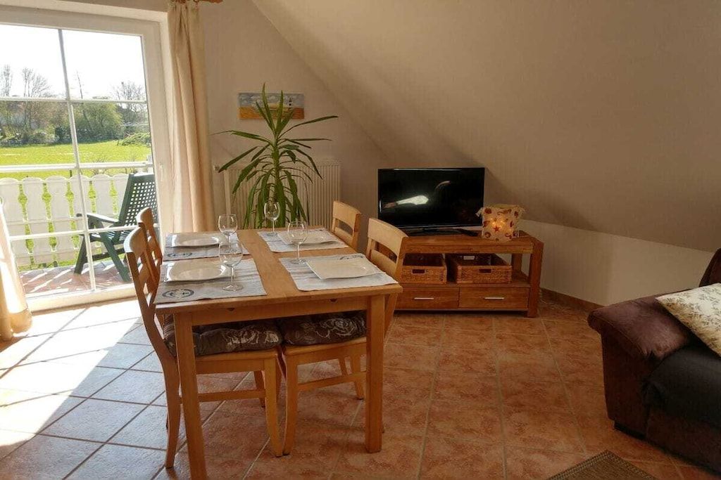 A dining area with a table set for two, a television on a stand, and a sofa in the corner.