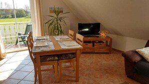 A dining area with a table set for two, a television on a stand, and a sofa in the corner. - Eckeberg with balcony (Hasselberg)