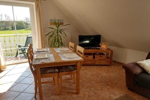 Ein Essbereich mit einem Tisch für zwei Personen, einem Fernseher auf einem Schrank und einer Couch in der Ecke.