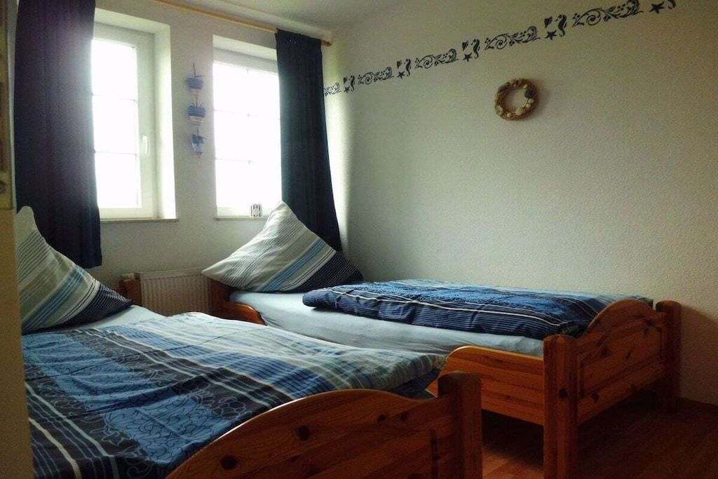 Une pièce avec deux lits en bois, une fenêtre avec des rideaux et un élément décoratif mural.