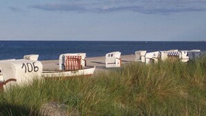 Beach chairs numbered 106 and 58, a white chair, and a row of beach chairs along a sandy beach with the ocean in the background. - Eckeberg with balcony (Hasselberg)