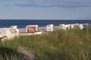 Strandliegen mit den Nummern 106 und 58, ein weißer Liegestuhl und eine Reihe von Strandliegen entlang eines Sandstrandes mit dem Meer im Hintergrund.
