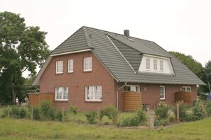 A two-story brick house with a sloped roof, a wooden gate, and a fenced yard. - Eckeberg with balcony (Hasselberg)