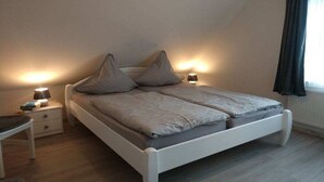 A bedroom with a bed, bedside tables, lamps, and a window with curtains. - Eckeberg with balcony (Hasselberg)