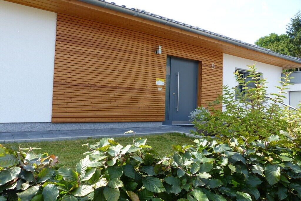 A modern building with a wooden facade, a grey door, and a small sign above the door.