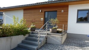 Een modern gebouw met een houten gevel, een aantal betonnen treden die naar een deur leiden met het nummer 8, en een parkeersbord.