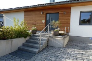 A modern building with a wooden facade, a set of concrete steps leading to a door marked with the number 8, and a parking sign. - Holiday home with 2 bedrooms (Wernigerode)