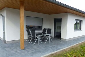A covered patio with a table and chairs, a wooden post, and a window with blinds. - Holiday home with 2 bedrooms (Wernigerode)