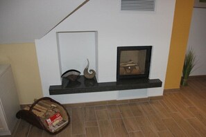 Eine Ecke mit Kamin, einer kleinen Ablage mit Dekoration und einem Holzvorrat auf dem Boden.