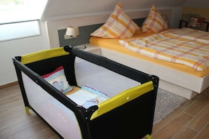 A child's playpen with a book inside, a bed with a yellow and white checkered bedspread, and a nightstand with a lamp. - Holiday apartment with 2 bedrooms (Sellin)