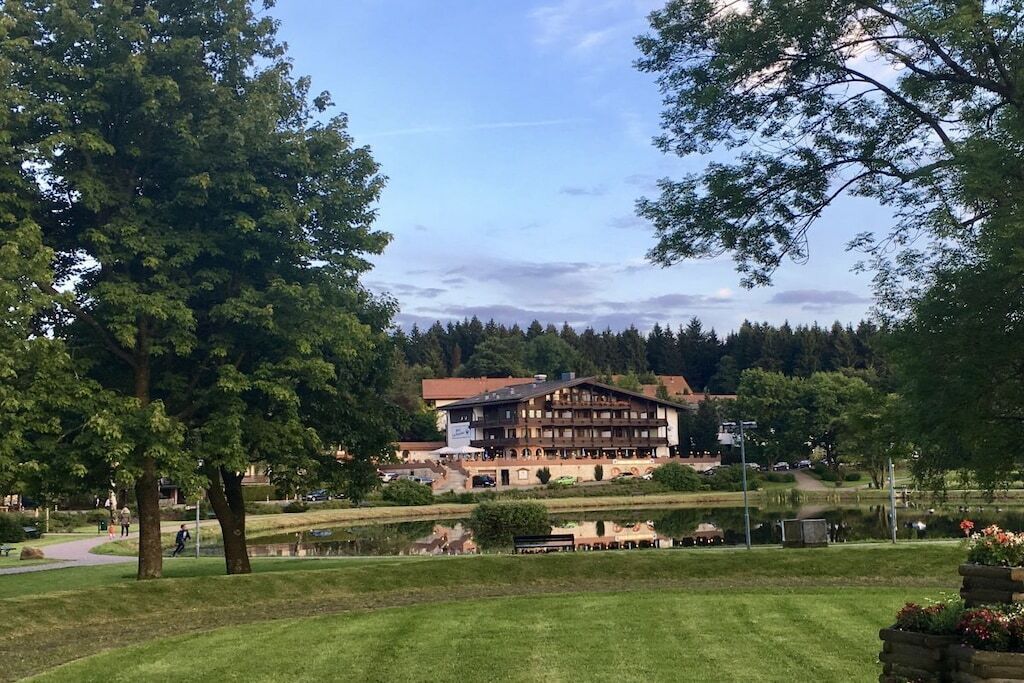 A hotel with a traditional chalet-style building, a well-maintained lawn, and a lake in the background.