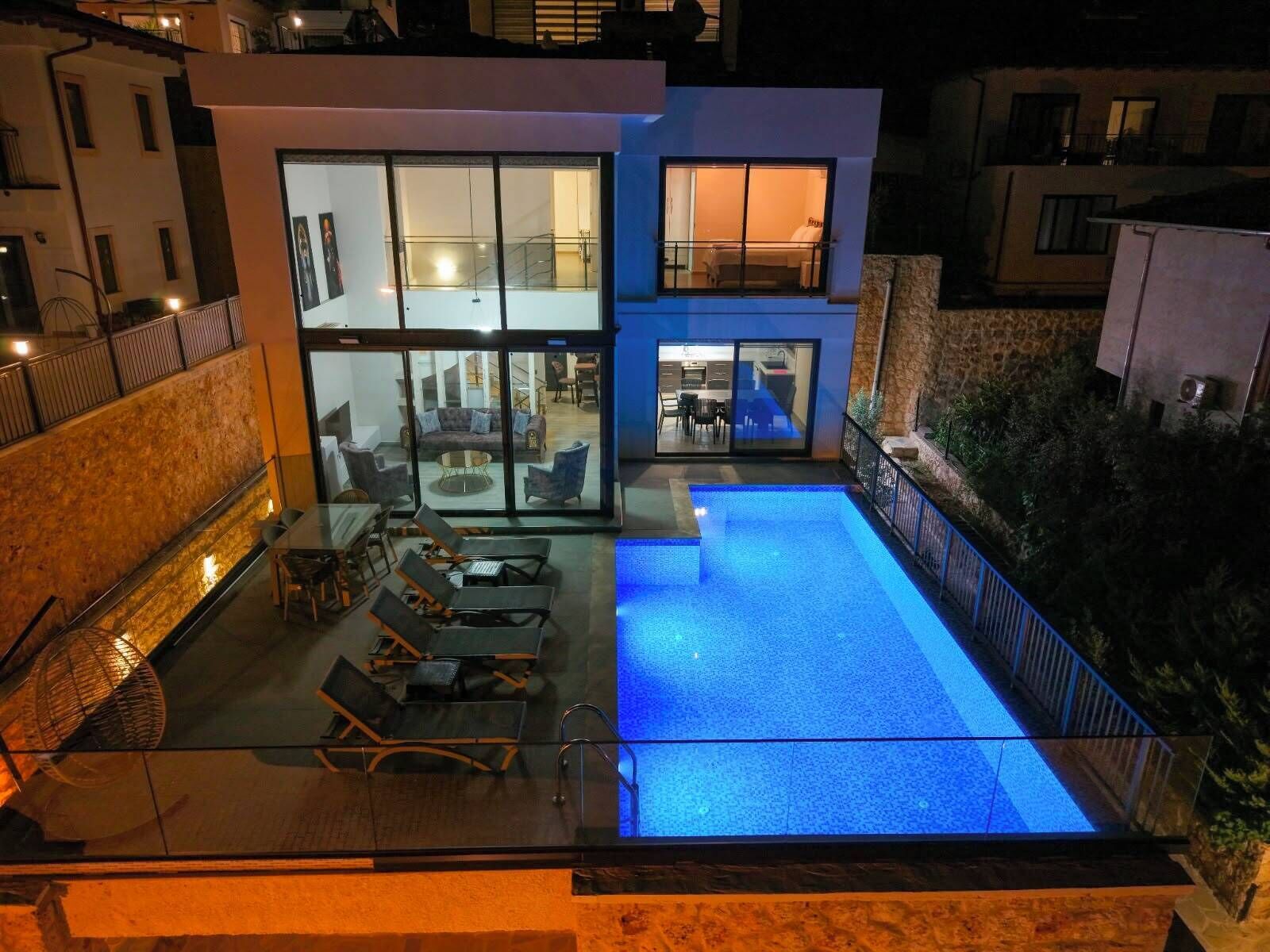 Une maison moderne dotée d’un patio entièrement vitré, d’une piscine et d’un espace repas aménagé avec du mobilier d’extérieur.