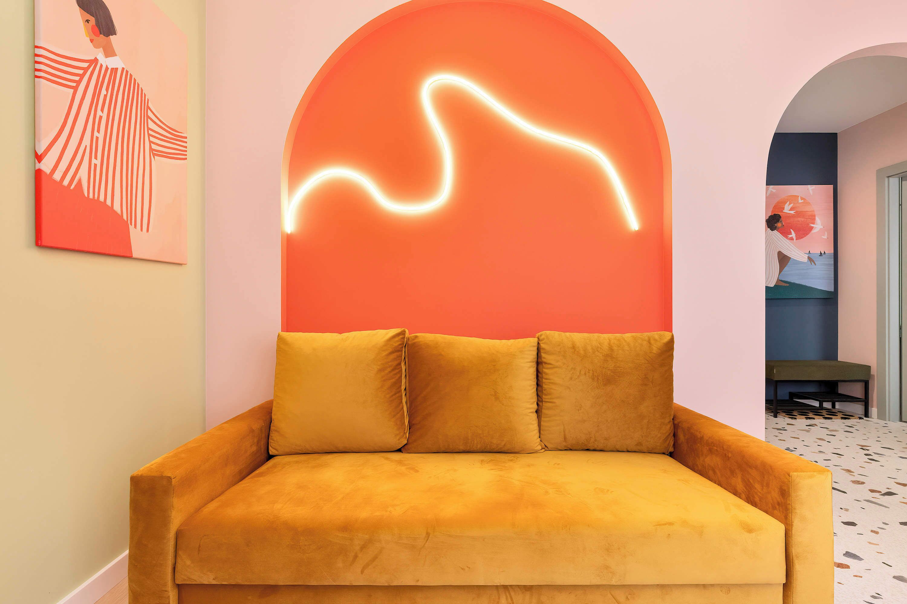Une pièce avec un canapé, un mur orné d’un motif lumineux au néon et un tableau.