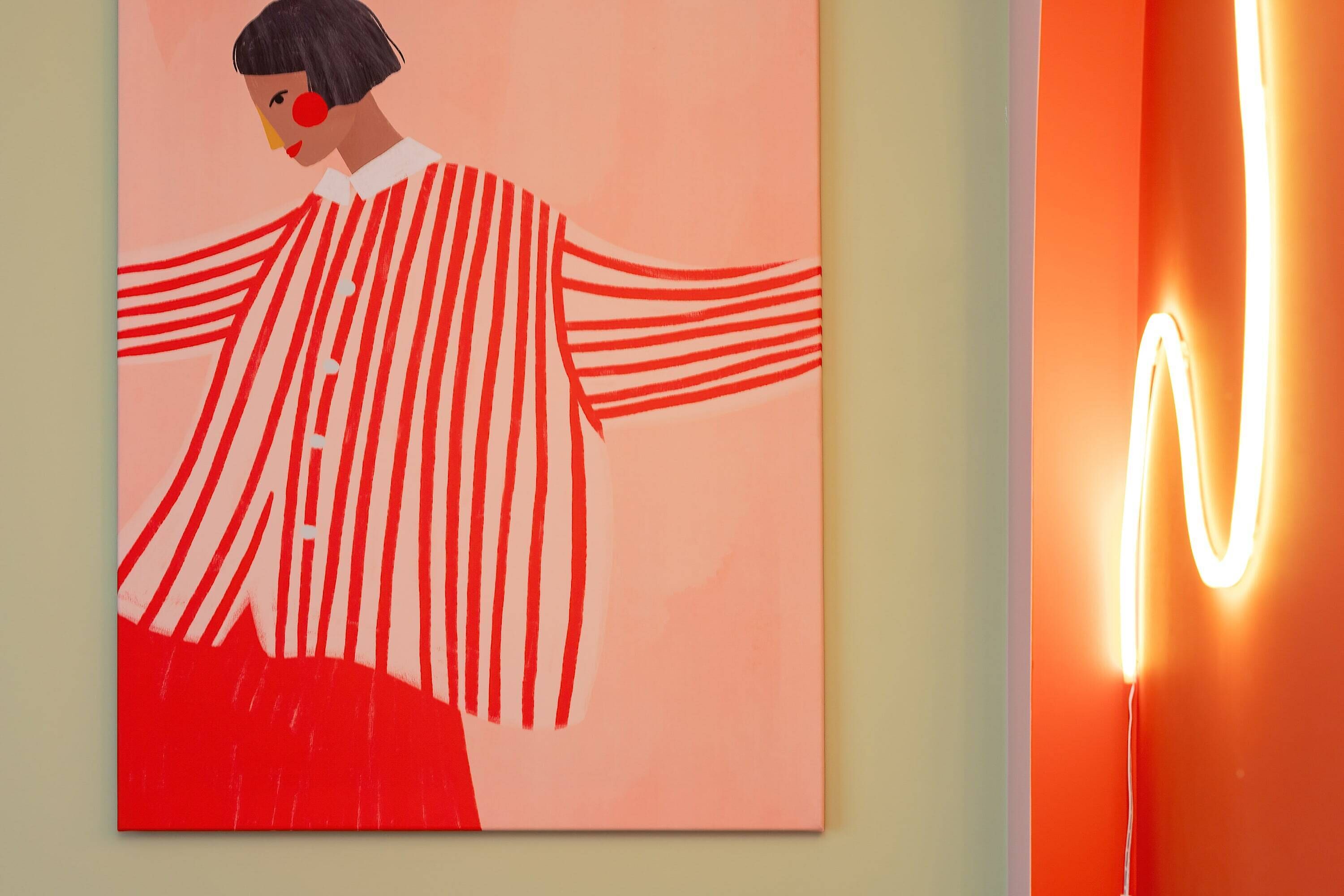 Pintura de una figura con los brazos extendidos sobre una pared, junto a una lámpara moderna.