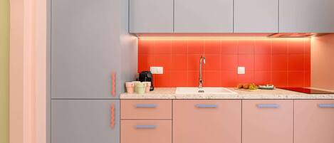 A modern kitchen with a grey refrigerator, a sink with a red backsplash, and a countertop with a coffee maker and cups.