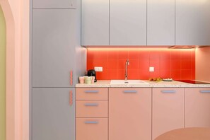 Una cucina moderna con frigorifero grigio, lavello con schienale rosso e un piano di lavoro con macchina da caffè e tazze.