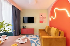 Ein modernes Wohnzimmer mit einer Couch, einem Fernseher, einem rosafarbenen Schrank und einem Essbereich mit Tisch für zwei Personen.