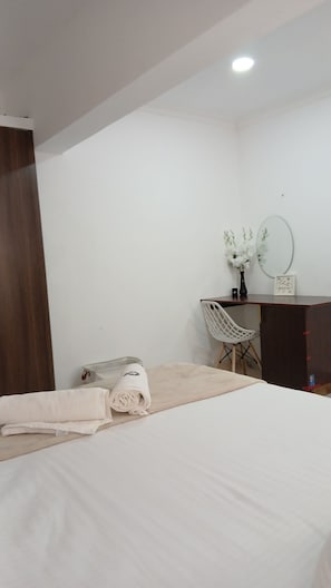 A hotel room with a bed, a desk, a chair, a mirror, and a wall-mounted light fixture. - One bedroom at the shores of Diani beach kenya (Kwale County)