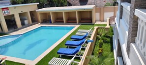 A swimming pool with lounge chairs, a covered seating area, and a warning sign. - One bedroom at the shores of Diani beach kenya (Kwale County)
