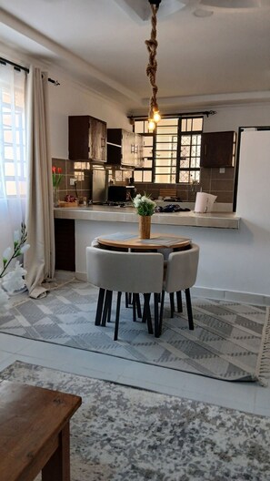 A modern kitchen with a central island, a dining area with a round table, and a hanging light fixture. - One bedroom at the shores of Diani beach kenya (Kwale County)
