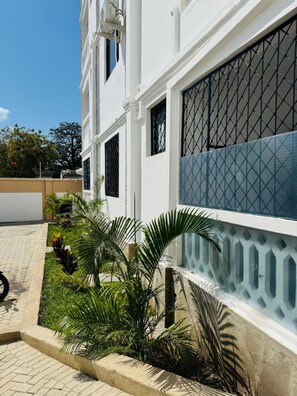 Ein Gebäude mit weißer Fassade, mehreren Fenstern mit schwarzen Gitterstäben und einem blau gemusterten Zaun.