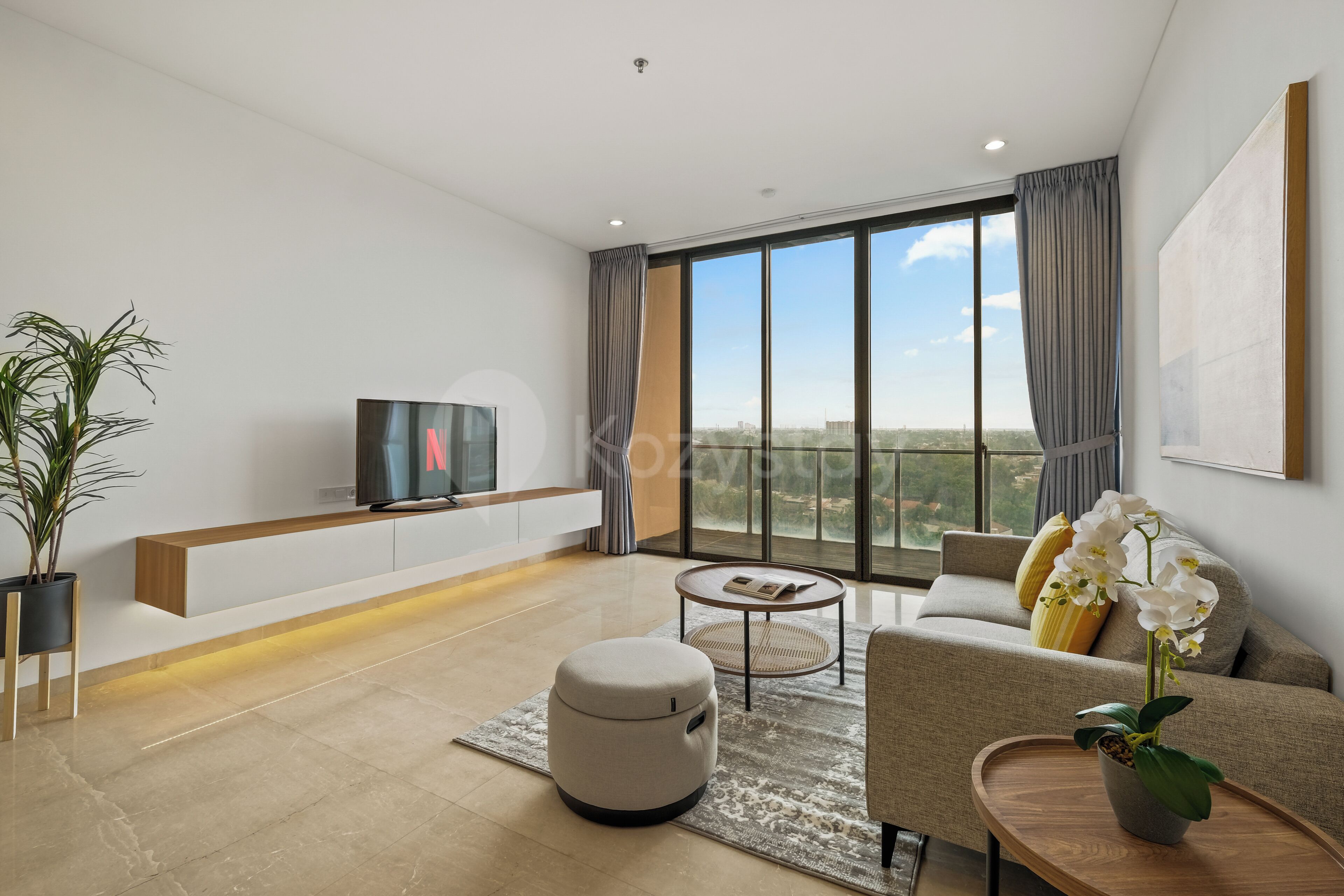 A modern living room with a flat-screen TV, a sofa, a coffee table, and a large window offering a city view.
