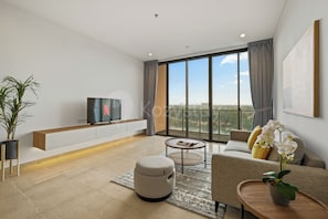 Ein modernes Wohnzimmer mit Flachbildfernseher, einer Couch, einem Couchtisch und einem großen Fenster mit Blick auf die Stadt.