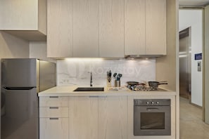 Eine moderne Küche mit hellen Holzschränken, einem Edelstahlkühlschrank, einem eingebauten Backofen und einer Spüle mit Marmor-Spritzschutz.