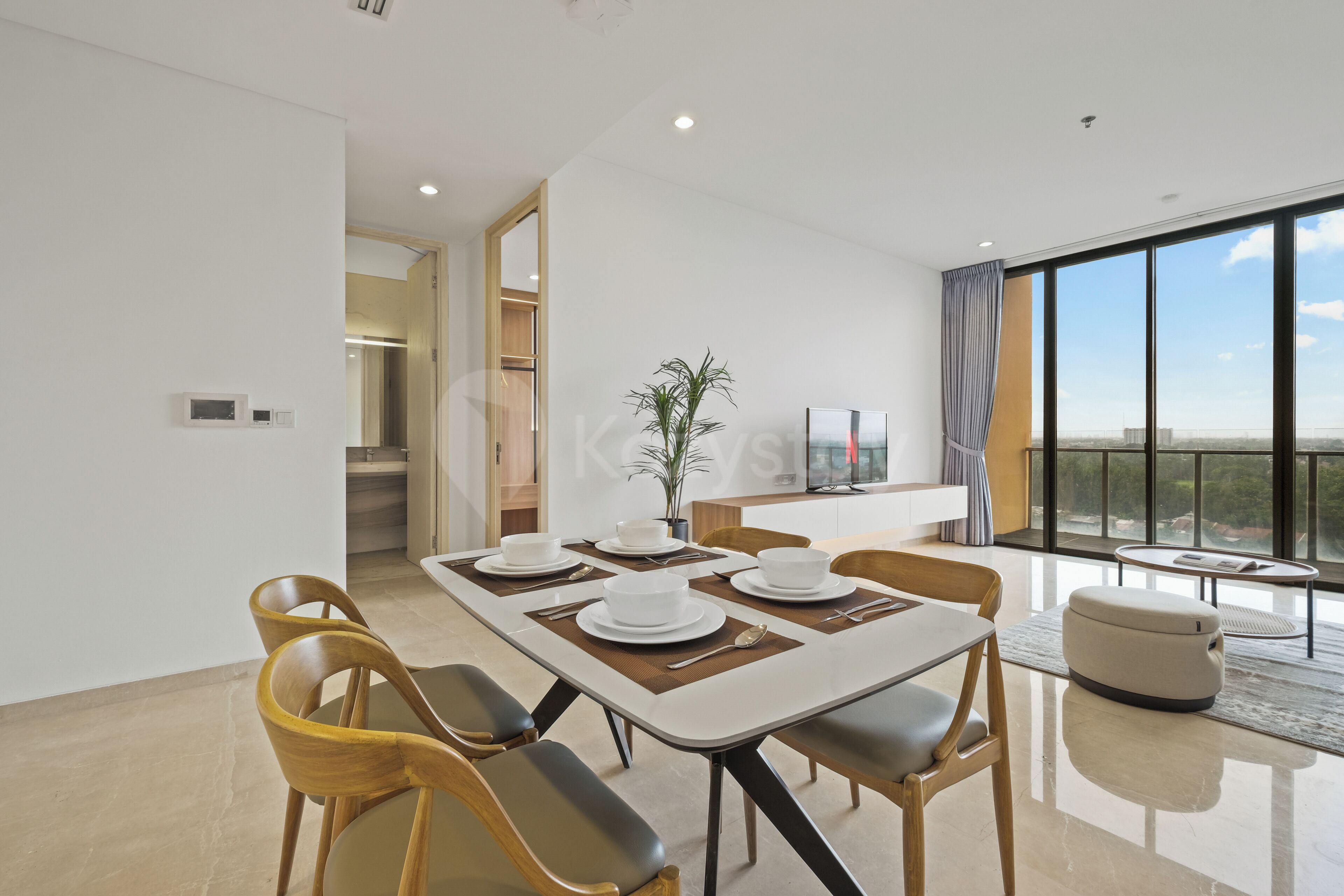A modern dining area with a large table set for four, surrounded by chairs, and a view of the city through large windows.