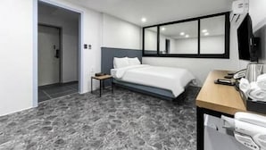A modern hotel room with a bed, bedside table, and a desk with a chair.