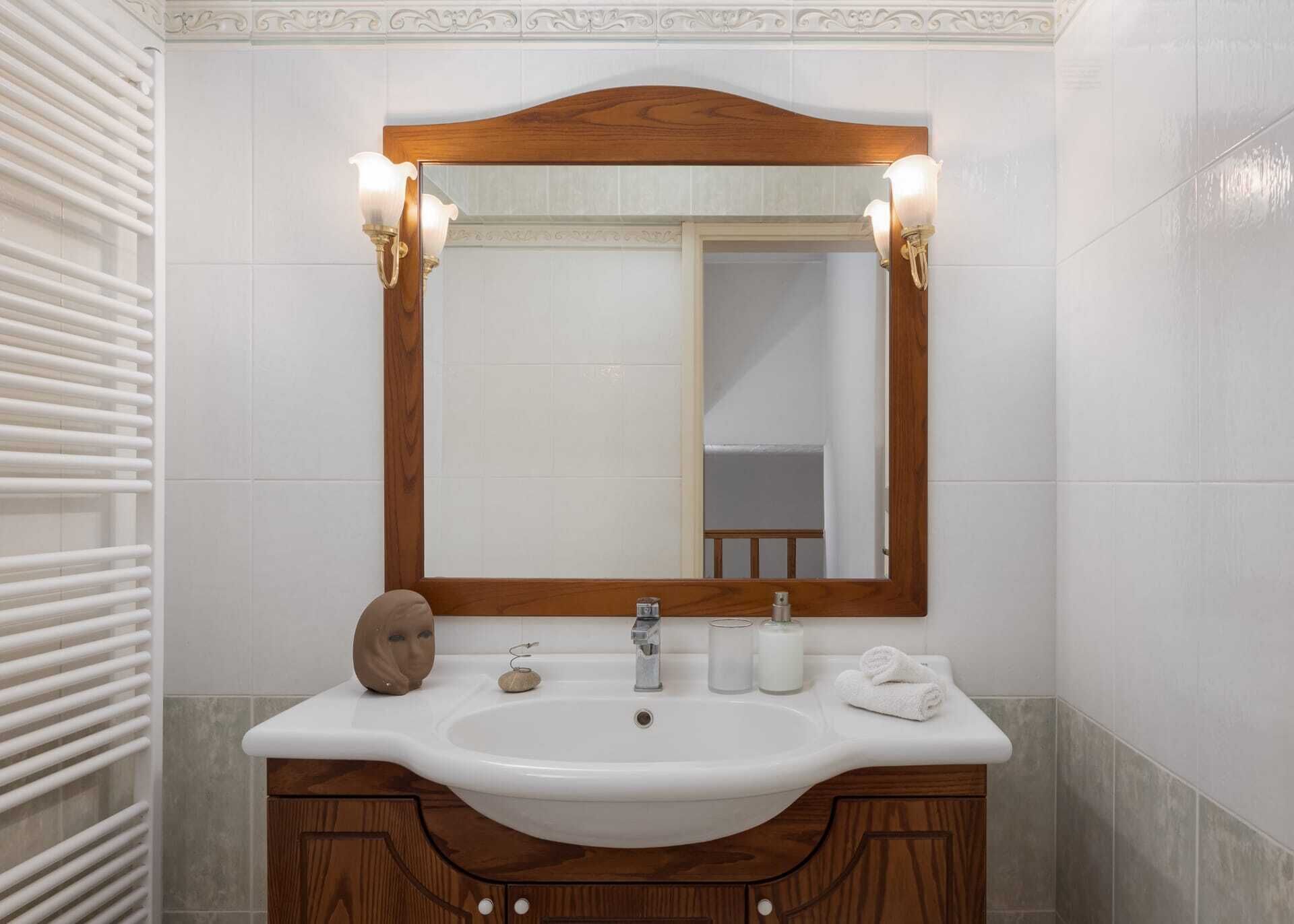 A bathroom with a wooden vanity, a mirror with wall sconces, and a towel rack.