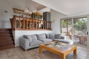 A living room with a grey sofa, a wooden coffee table, and a staircase leading to a balcony. - Melitta Villa Aegina, Villa (Aegina)