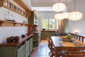 A kitchen with wooden cabinetry, a dining table with chairs, and pendant lights. - Melitta Villa Aegina, Villa (Aegina)