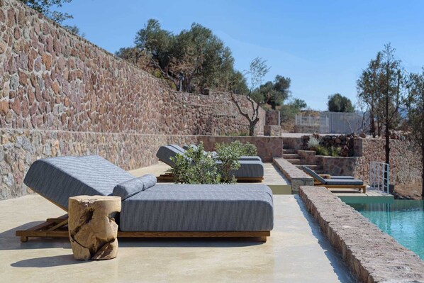 A poolside area with stone walls, lounge chairs, and a small plant. - Melitta Villa Aegina, Villa (Aegina)