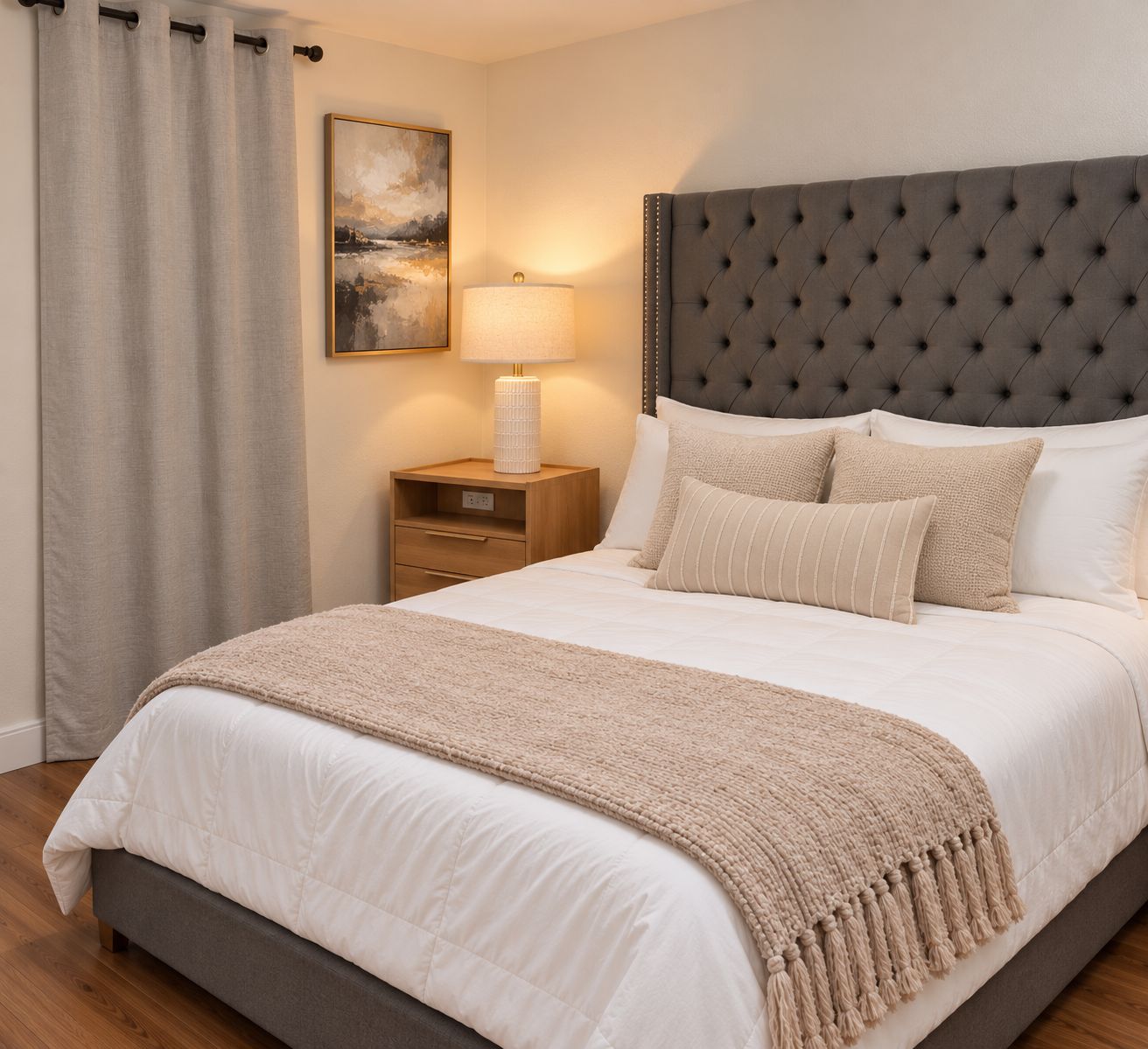 A bedroom with a large bed, a nightstand with a lamp, a headboard, and a painting on the wall.