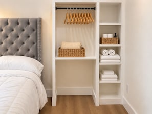 A bedroom with a tufted headboard, a wardrobe with hanging space, shelves with towels, and a bed with white bedding. -     Modern 4BR/4BA Townhome w/ Rooftop Near Downtown Dallas (Dallas)