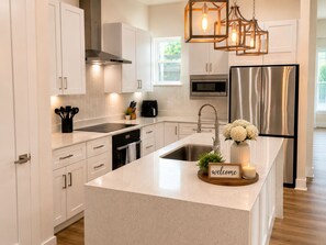 A modern kitchen with white cabinetry, a stainless steel refrigerator, a built-in oven, and a central island with a 'welcome' sign. -     Modern 4BR/4BA Townhome w/ Rooftop Near Downtown Dallas (Dallas)
