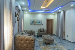 A modern living room with a sofa, armchair, ottoman, and a painting on the wall. - Stallion Luxury Suites (Abuja)