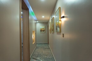 Um corredor com piso de mármore, portas de madeira e luminárias fixadas na parede.