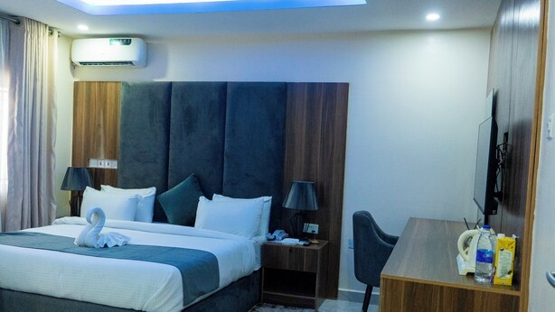 Habitación de hotel con cama, lámparas de noche, escritorio, silla, televisor de pantalla plana y unidad de aire acondicionado.