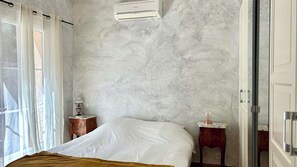 Ein Schlafzimmer mit einem Bett, einem Nachttisch, einer Lampe und einer Klimaanlage an der Wand.